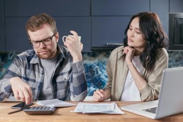 A focused young couple reviewing documents and managing their budget at home, showcasing modern financial challenges.