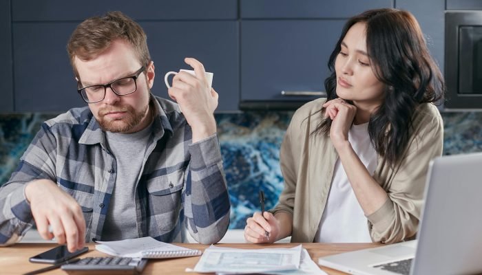 A focused young couple reviewing documents and managing their budget at home, showcasing modern financial challenges.
